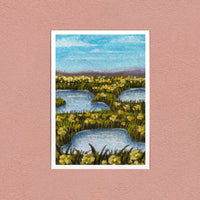 Flower Meadow in Orange art print — orange-gold wildflowers around blue pools, shown on a pink wall